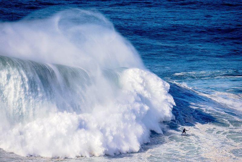 Une vague gigantesque se brise juste derrière la silhouette minuscule d'un surfer.
