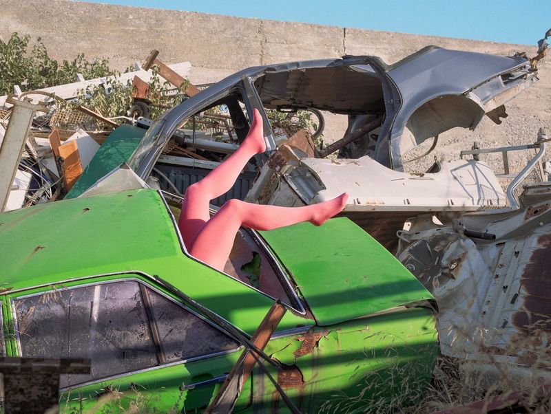 Une paire de jambes vêtues de collants roses surgit de la fenêtre arrière d'une voiture abandonnée vert citron.
