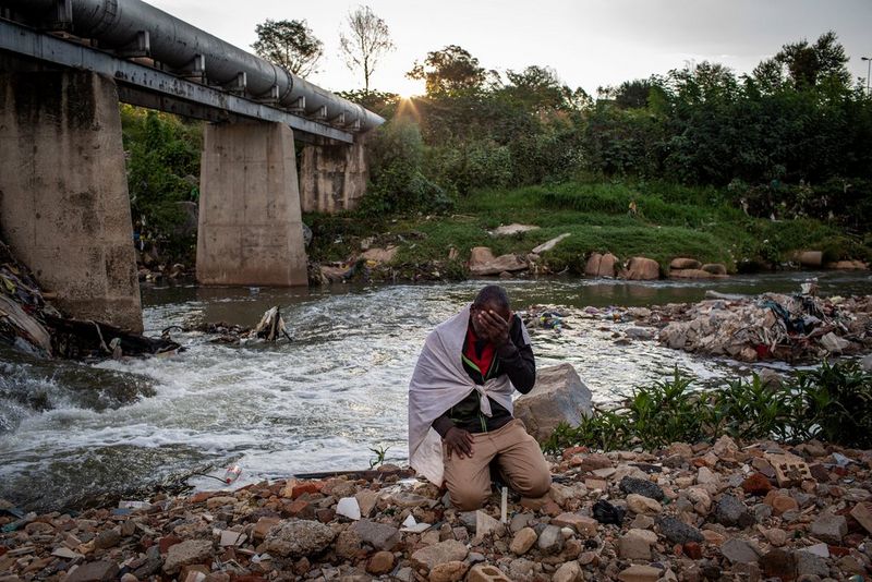Un homme enveloppé dans un drap blanc est agenouillé et prie sur le bord de la rivière Jukskei en Afrique du Sud.