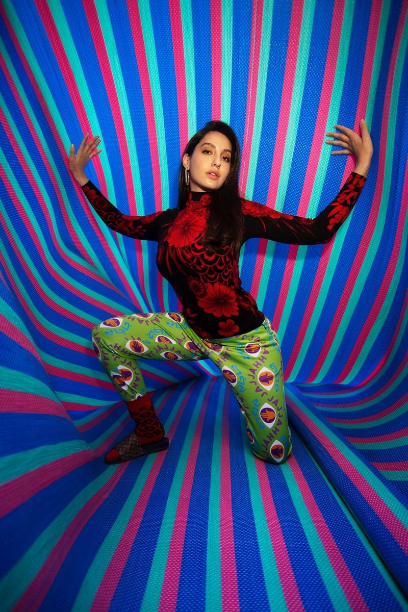 Une jeune femme portant des vêtements flamboyants pose devant un fond rayé coloré.