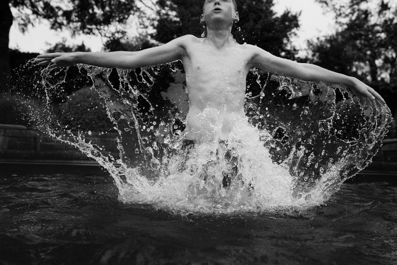 Image en noir et blanc d'un garçon sautant hors d'une piscine, éclaboussant d'eau tout ce qui se trouve autour de lui.