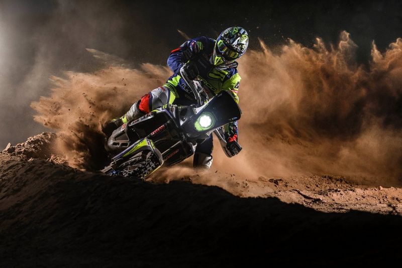 Un motocycliste effectue un virage sur une piste boueuse, soulevant un énorme nuage de poussière.