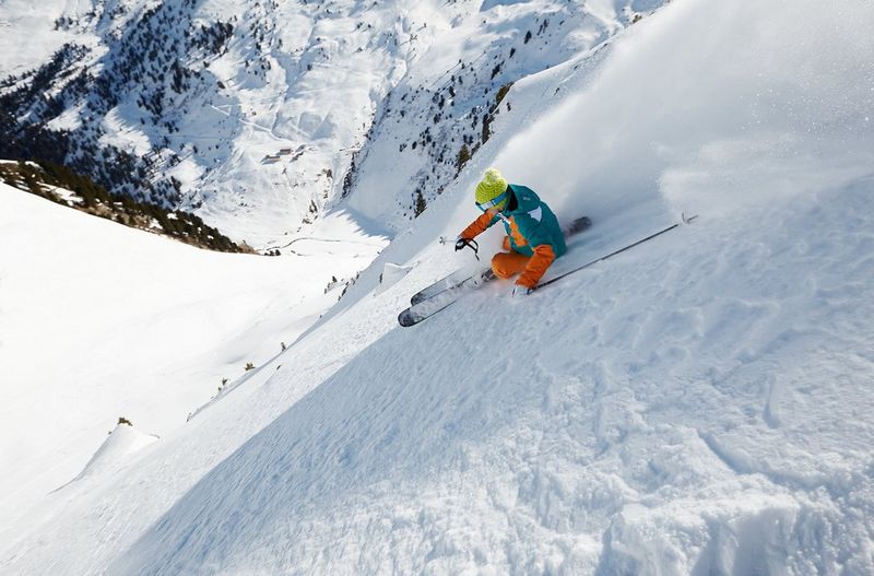Une femme portant des vêtements de couleurs vives skie habilement sur une montagne escarpée.