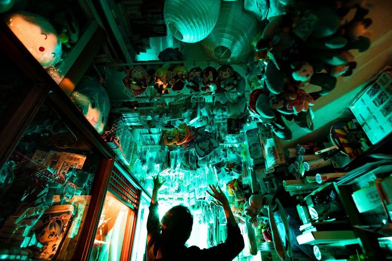 Silhouette d'un homme qui lève le bras vers le plafond de son appartement, rempli de figurines de Hatsune Miku.