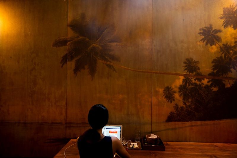 Une femme travaille dans un espace de co-working à Canggu, à Bali. Sur le mur en face d'elle se trouve l'image d'une plage paradisiaque.
