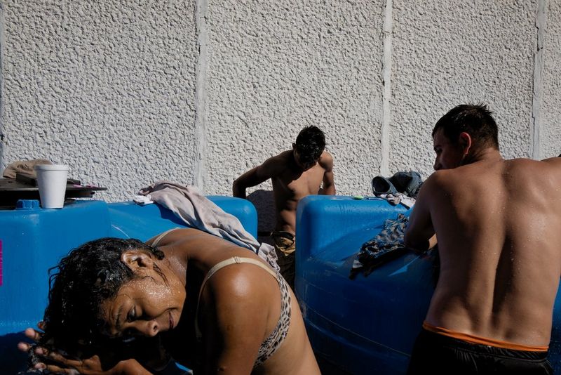 Trois migrants honduriens, une femme et deux hommes, se lavent avec des moyens limités dans le stade de baseball Jesús Martínez Palillo à Mexico en 2018 lors d'une pénurie d'eau.
