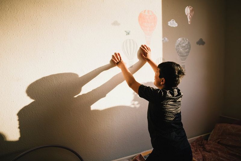 Un jeune garçon joue avec son ombre, adossé à un mur décoré de montgolfières dessinées au pochoir.