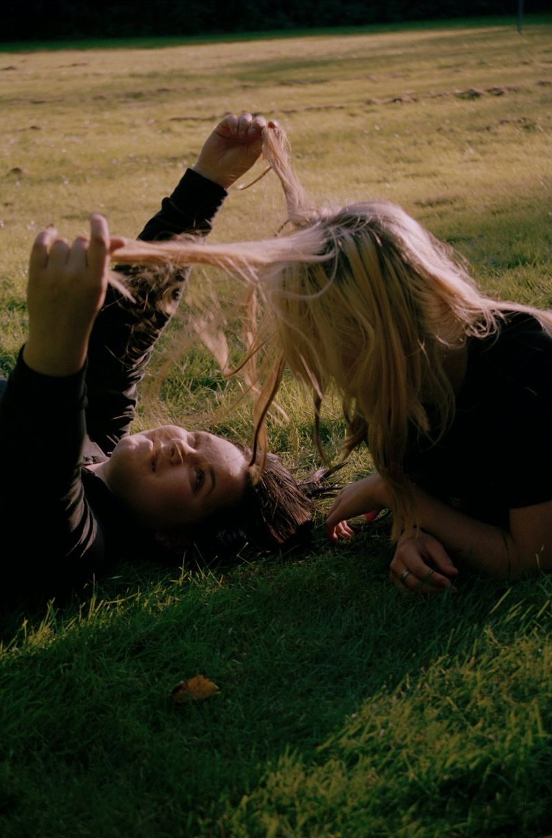 Deux jeunes filles allongées sur un champ d'herbe jouent avec leurs cheveux.