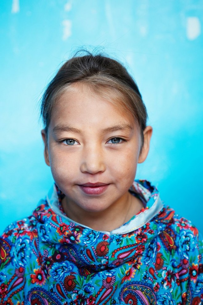 A young Siberian girl in a colourful jumper smiles for the camera. 