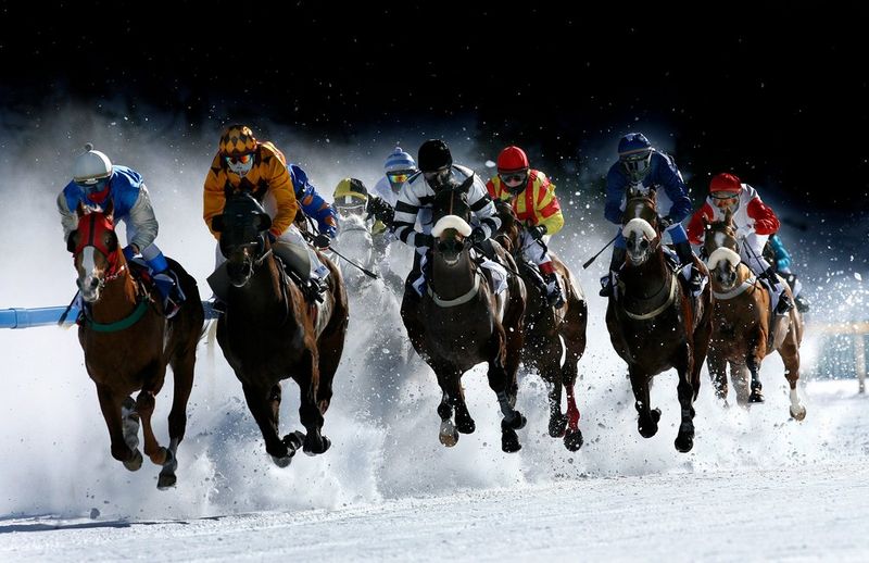 Des jockeys au galop et au coude à coude sur une piste couverte de neige. La neige vole en dessous et autour des sabots des chevaux.