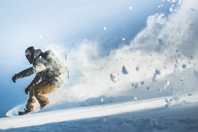 Pushing the left edge of the frame, a snowboarder kicks up fresh powder behind them.