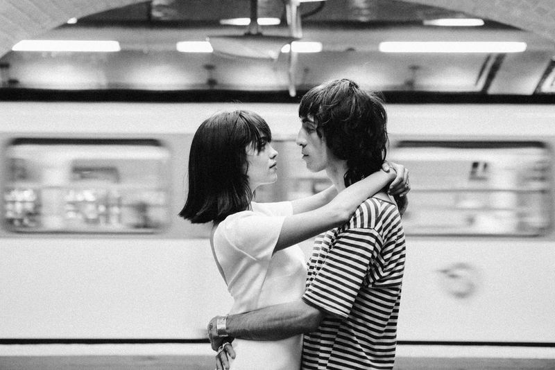Image en noir et blanc d'un homme et d'une femme en pleine étreinte sur une plateforme du métro parisien. Derrière eux, un train passe à toute allure.
