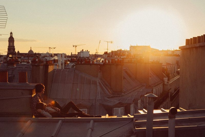 Une femme se repose entre les jambes d'un homme assis sur un toit surplombant un paysage urbain.