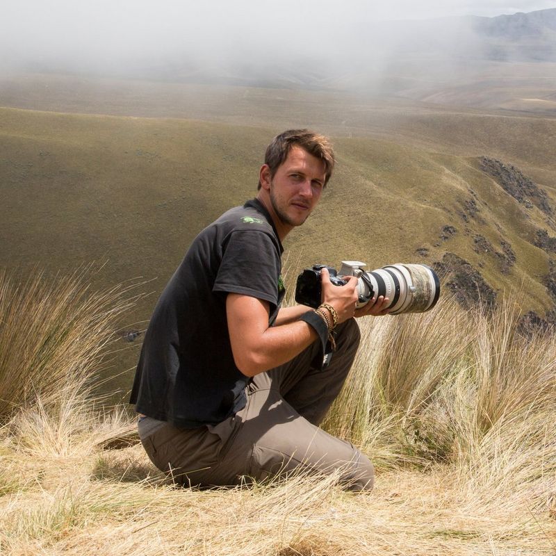 Canon Ambassador Maxime Aliaga on a grassy hilltop holding a Canon camera with a Canon telephoto lens.