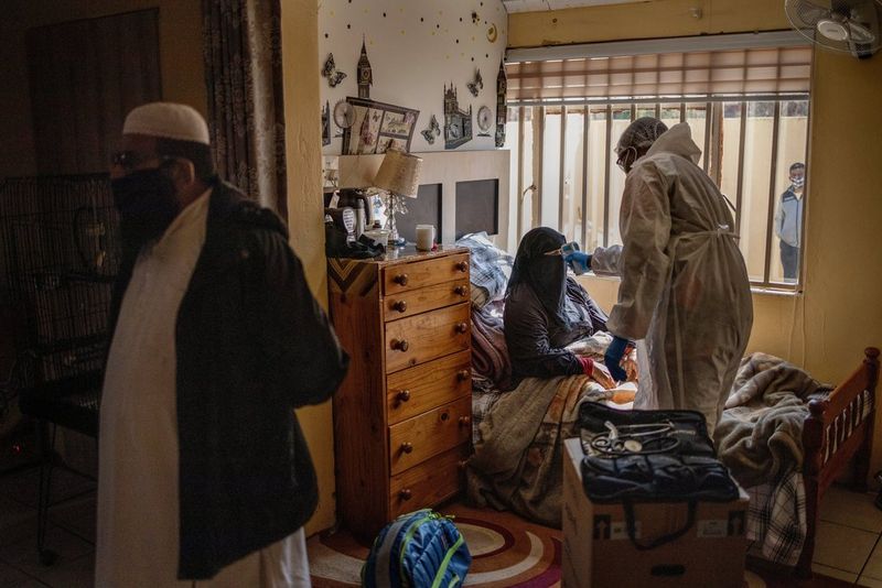 Un auxiliaire médical vêtu d'une tenue de protection prend la température d'une femme portant un niqab.