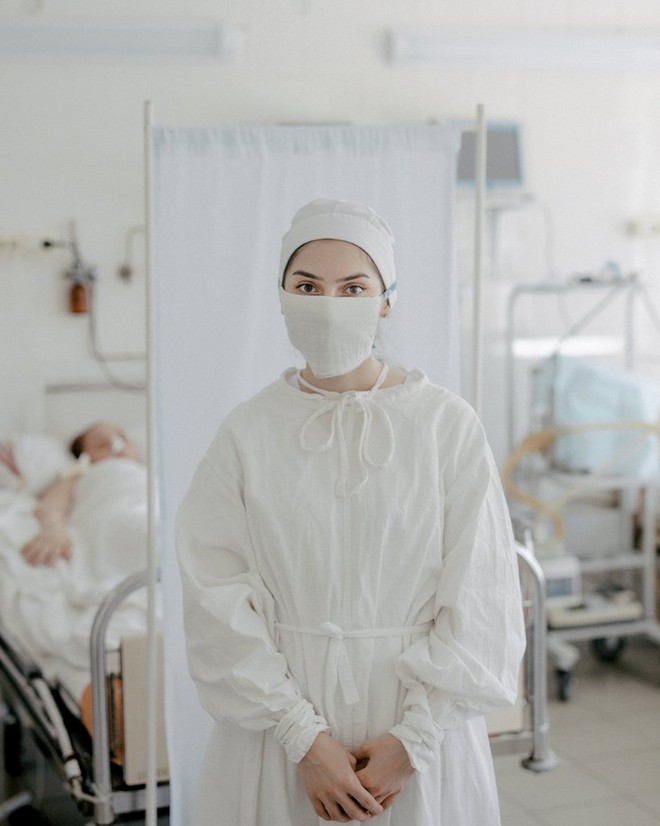 A female nurse wearing personal protective equipment stands in front of patients' beds in a Russian hospital. 