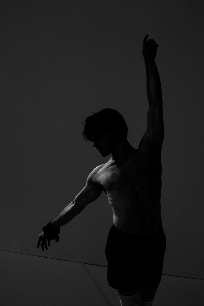 Photo en noir et blanc d'un danseur de ballet avec un bras levé et l'autre tendu.