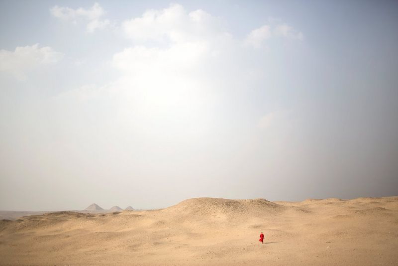 Une minuscule silhouette en robe rouge traverse le désert sous un soleil de plomb.