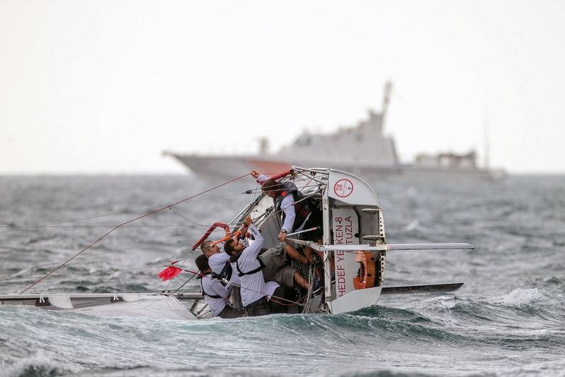 Un bateau en train de chavirer en mer avec la voile à plat contre l'eau et l'équipage essayant de le redresser.