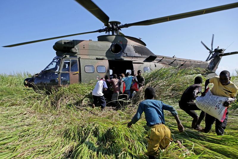 Des hommes transportant des sacs de riz depuis un hélicoptère qui a atterri sur un champ d'herbe.