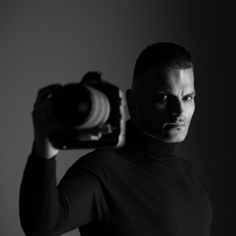 A black-and-white headshot of Canon Ambassador Sanjay Jogia holding his Canon camera.