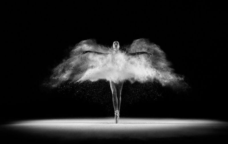 Une image en noir et blanc d'une ballerine figée dans le mouvement. La farine blanche jetée donne l'impression qu'elle a des ailes.
