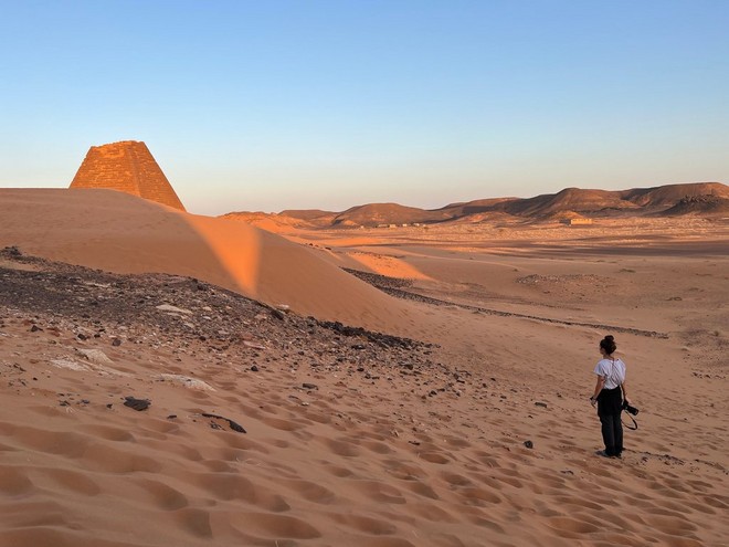 La Canon Ambassador Camilla Ferrari si trova tra le dune di sabbia del Sudan, una piramide con la sommità spezzata nelle vicinanze.