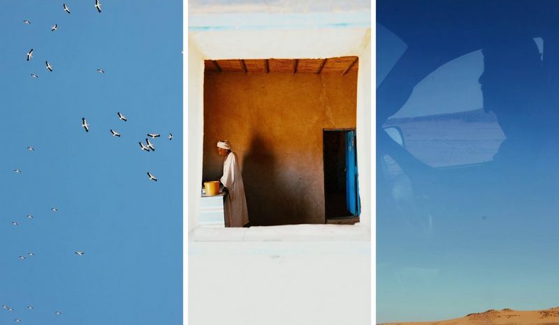 Un trittico di uccelli che volano attorno ad un cielo azzurro brillante; un uomo con lunghe vesti bianche in piedi accanto a un piano di lavoro, fotografato attraverso una finestra in un muro bianco; e il riflesso di un automobilista nel finestrino di un'auto, attraverso il quale si può vedere un cielo e una terra di un azzurro brillante. Scattato da Camilla Ferrari.