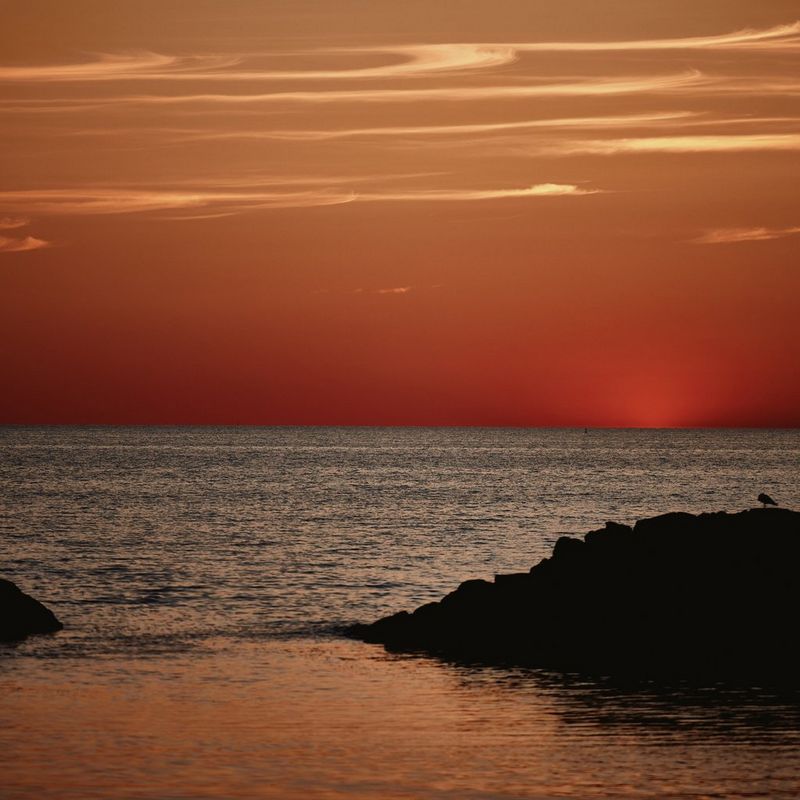 Waves lap gently at two rock formations against a burnt orange sky. 