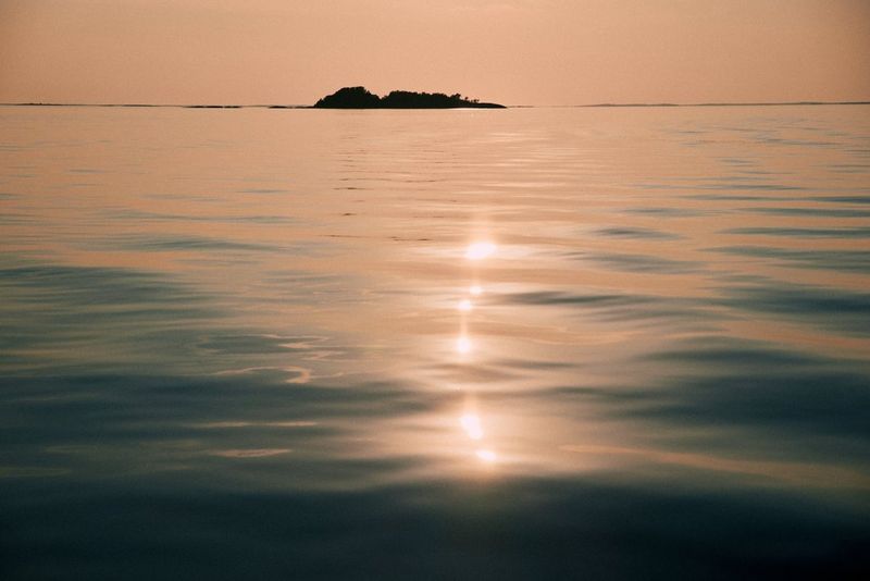 Des rayons de soleil illuminent un plan d'eau immobile. On aperçoit la silhouette d'une petite île en arrière-plan.