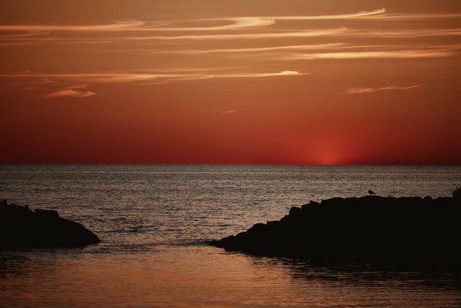 Les vagues clapotent doucement sur deux formations rocheuses contre un ciel orange brûlé.
