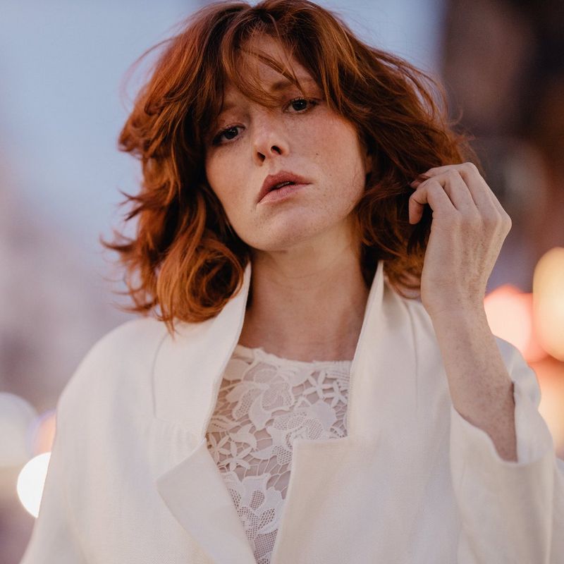 A portrait of a model in a white jacket in front of a busy but blurred street.
