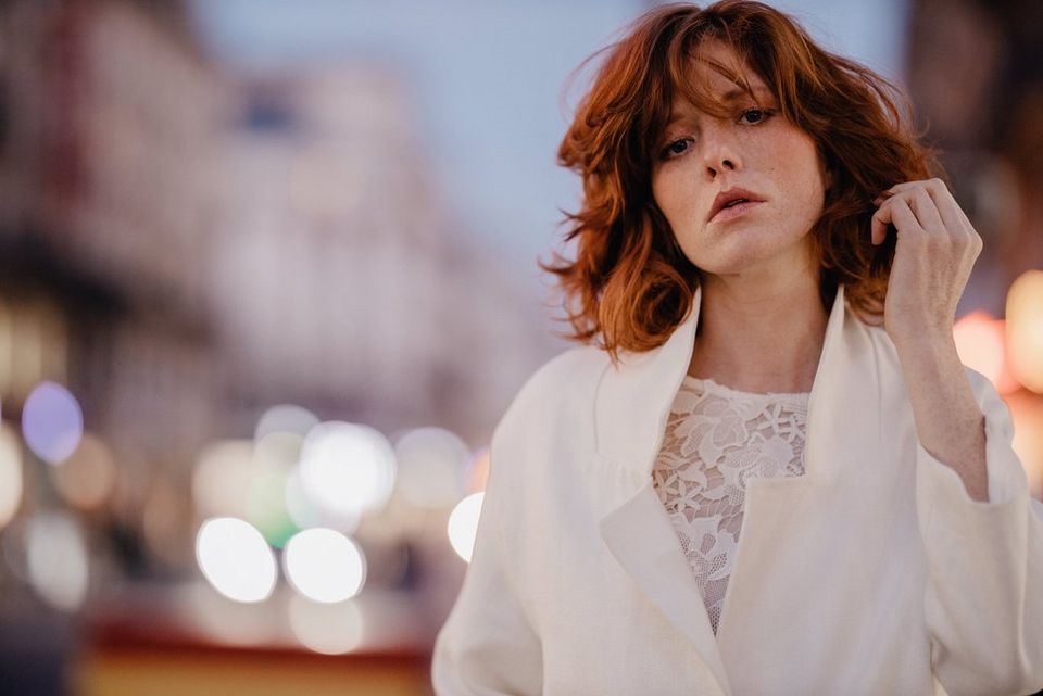 A portrait of a model in a white jacket in front of a busy but blurred street.