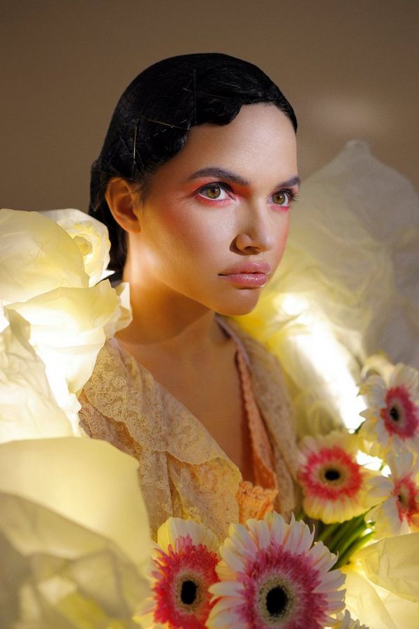 A close-up portrait of a model wearing a yellow outfit covered with flowers. 