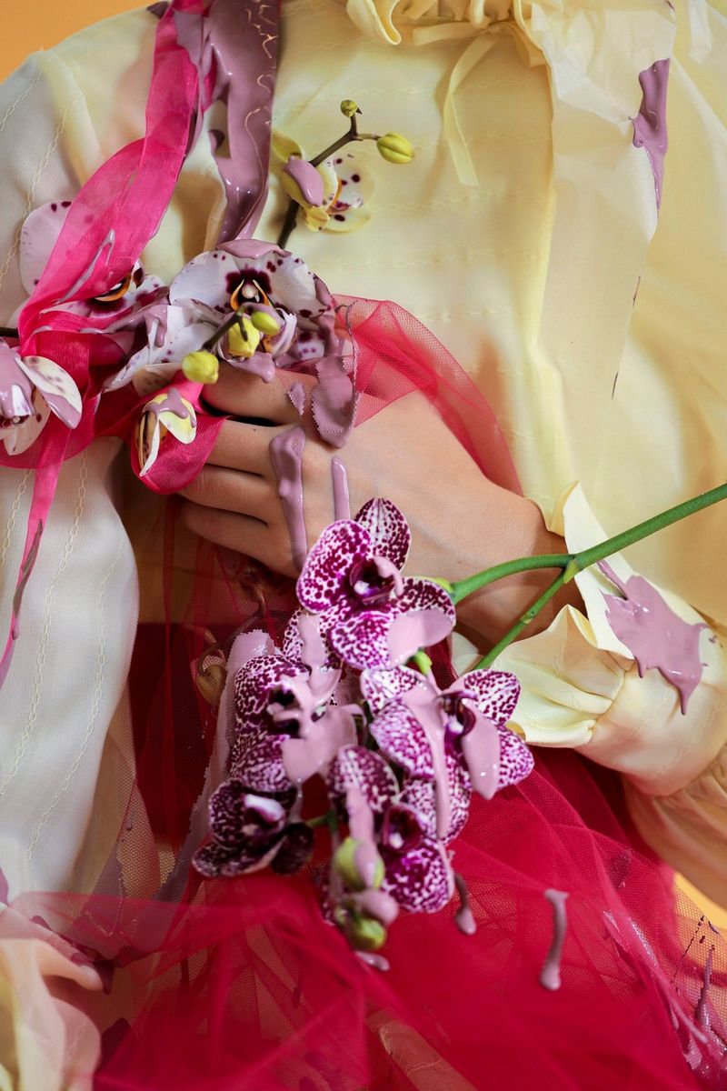 A close-up of a model’s hands and torso, draped in flowers. 