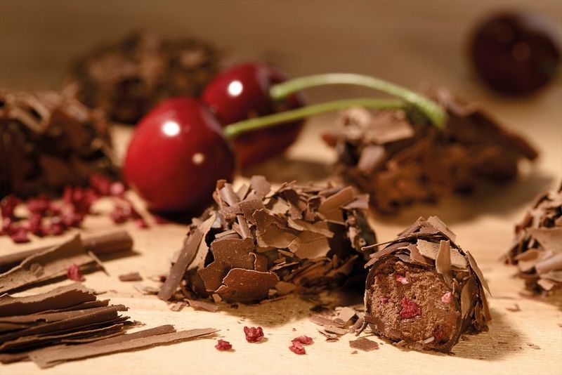 Gros-plan de truffes à la cerise recouvertes de copeaux de chocolat, avec deux cerises derrière.