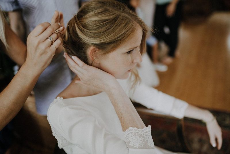 Une mariée dans sa robe blanche assise pendant qu'elle se fait coiffer pour le jour du mariage.