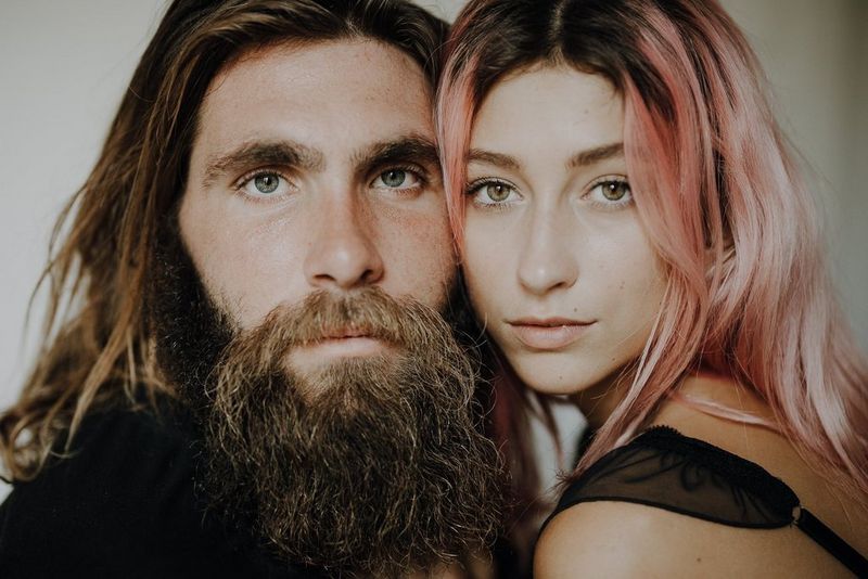 Portrait en gros plan d'un homme barbu avec de longs cheveux et d'une femme aux cheveux teints en rose, son visage tout près du sien.