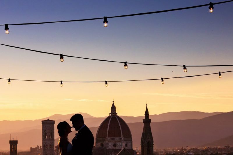 Silhouette d'un couple sur fond de soleil couchant à Florence, le Duomo derrière eux et les montagnes brumeuses en arrière-plan.