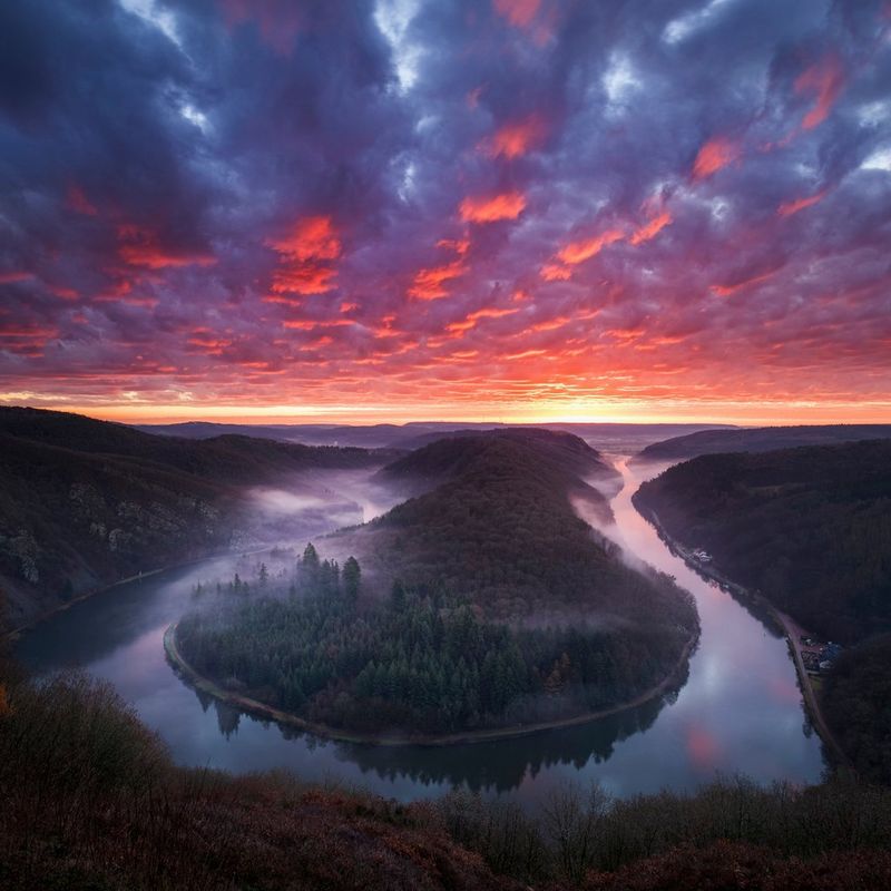 A meandering river surrounded by forest, shot under an orange and purple sky.