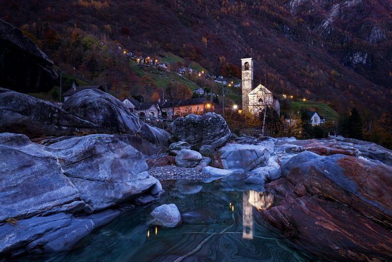 Église perchée dans les montagnes suisses, avec une rivière se frayant un chemin à travers les rochers au premier plan.