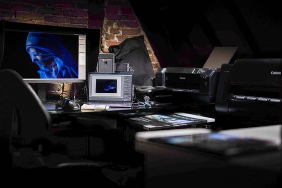 A professional home photography studio containing a laptop, a large screen showing a photograph of a woman in a blue veil, a Canon camera and several Canon printers. 