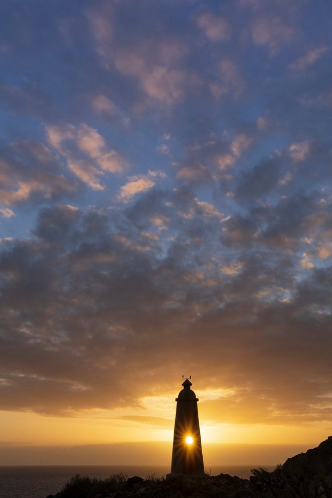 A silhouette of a lighthouse against a dimming yellow sky. 