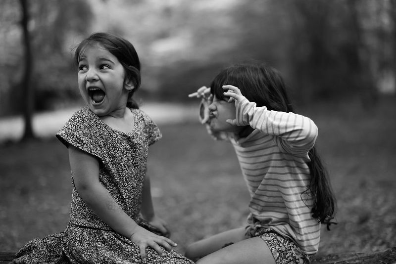 A black and white portrait of two young girls kneeling on the floor; one is pulling a scary face while the other shrieks in mock fear.
