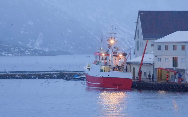 A fishing boat moored next to a row of wooden buildings in a snowstorm.