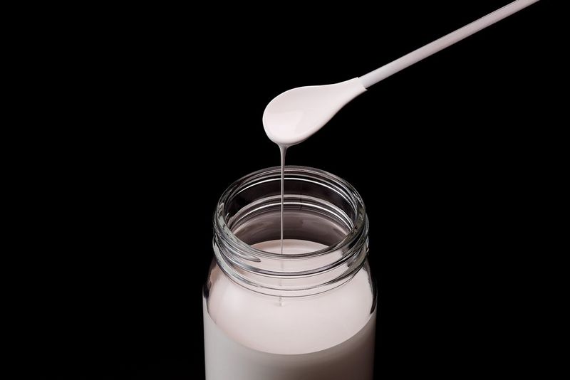 A thick white liquid drips from a spatula into a jar.