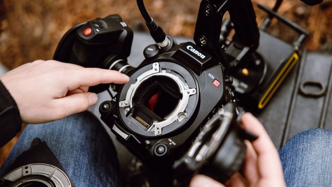 Twee handen houden een Canon Cinema EOS-camera vast en één ervan wijst naar een full-frame sensor in de camera.