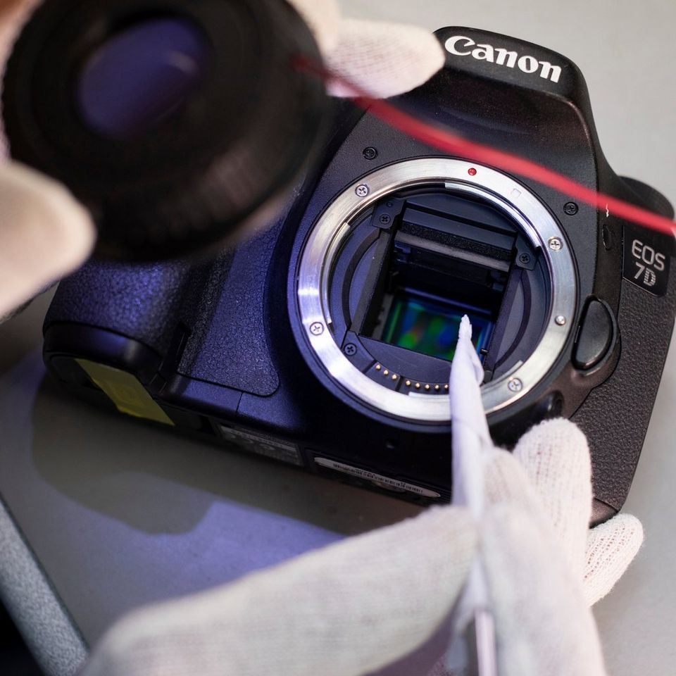A technician wearing white gloves cleans the sensor of a Canon camera.