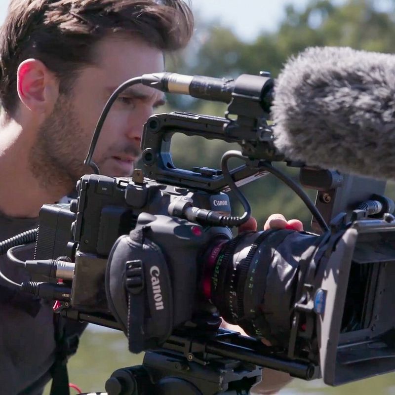 DoP Ben Sherlock filming with the Canon EOS C300 Mark III in a rural setting with bushes and water in the background.