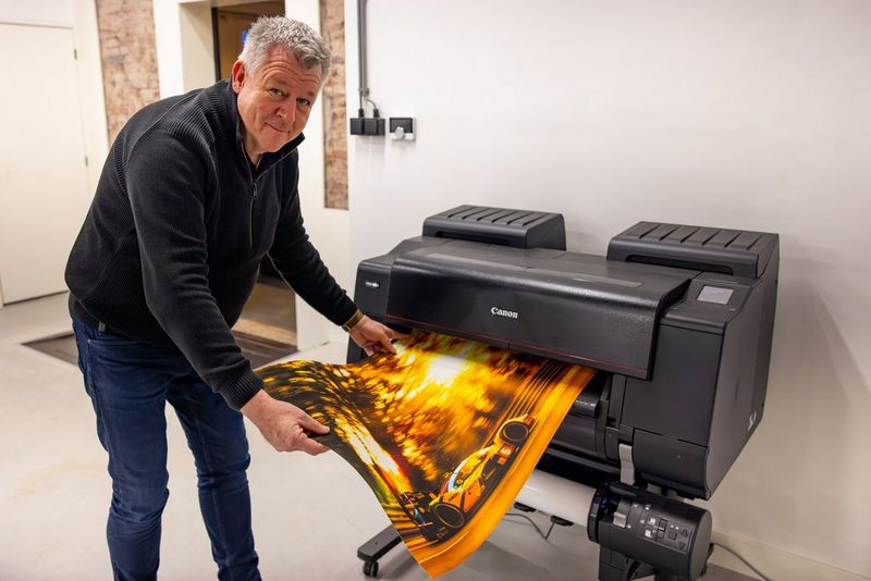 Motorsport photographer Frits van Eldik holds a large print of a vehicle as it emerges from a Canon large format printer.